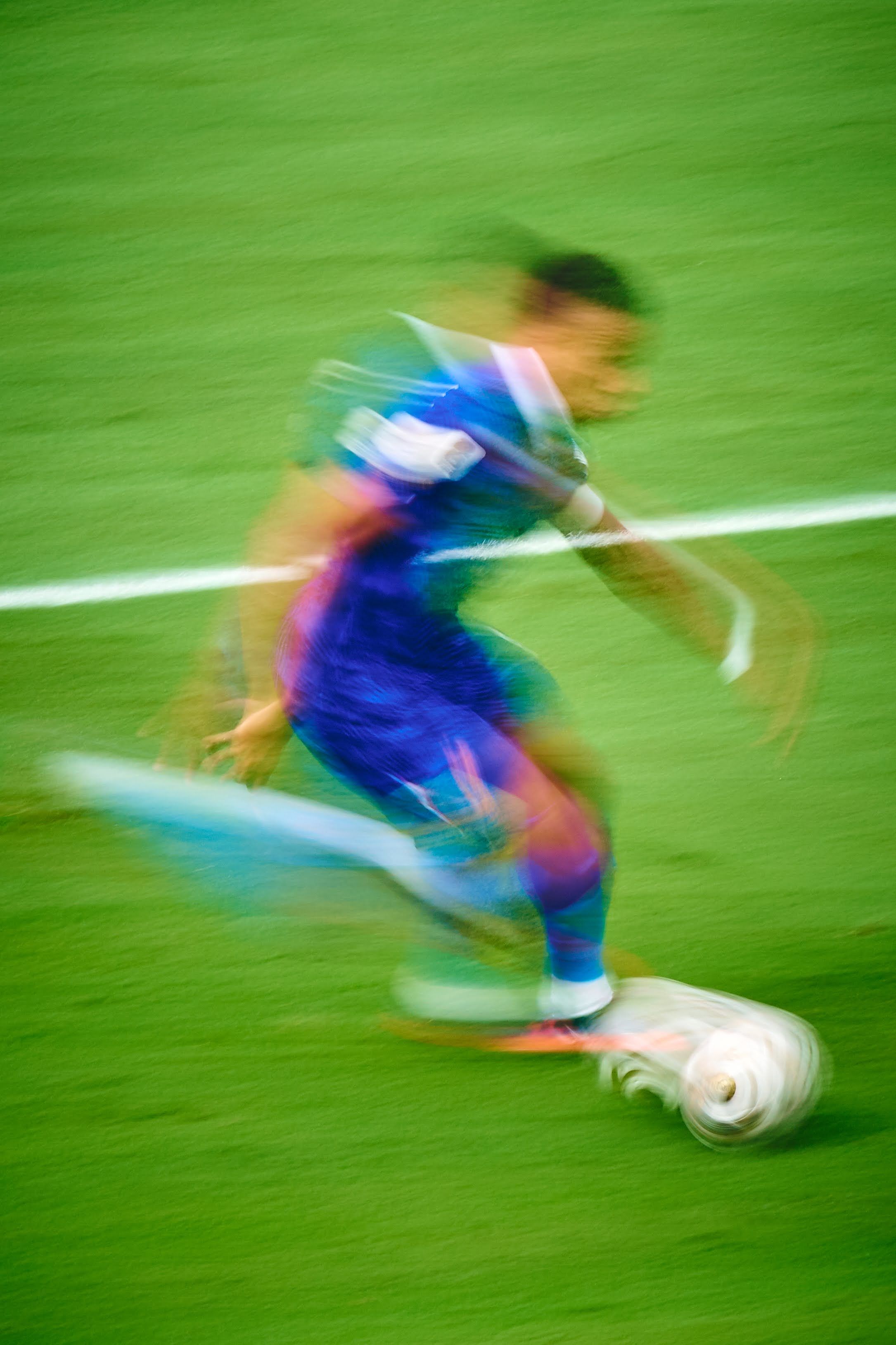 Blurred motion shot of a soccer player dribbling a ball on a green field, capturing speed and agility.
