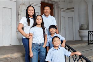 Family of five posing on steps of elegant building, parents with three children wearing matching blue and white outfits.