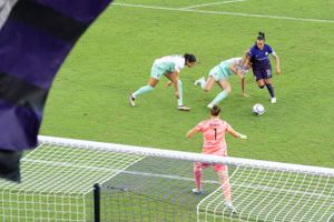 Soccer match action shot showing players and goalkeeper near the goal net.