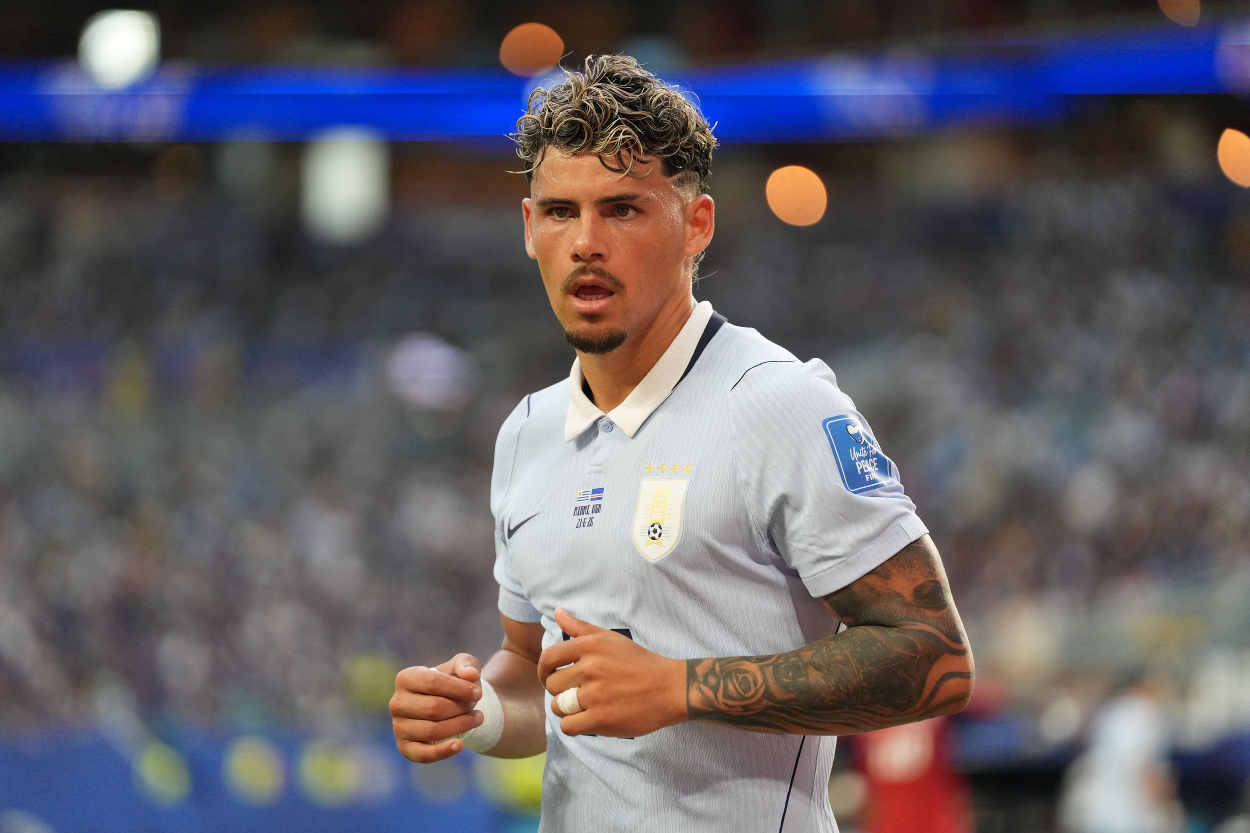 Soccer player in white jersey with tattoos jogging on field during a professional match at a stadium.