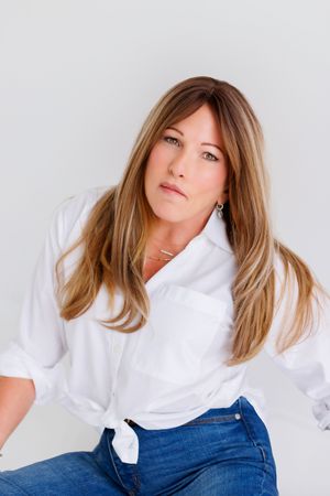 Woman in casual white button-down shirt and jeans poses against light background.