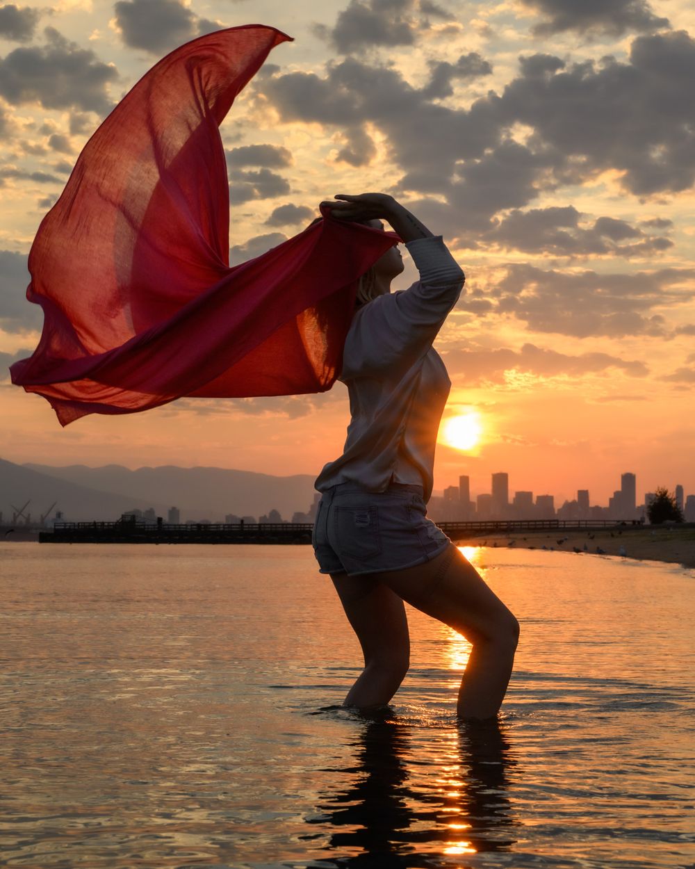 Woman with red scarf at sunset waterfront with Vancouver skyline, North Vancouver portrait photographer
