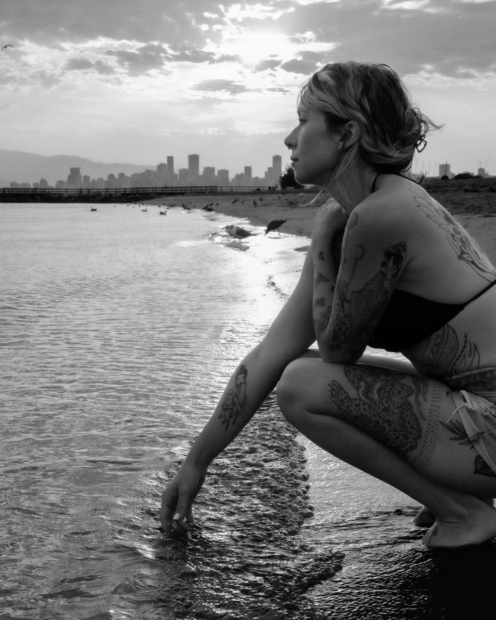Black and white portrait of woman crouching at water's edge, North Vancouver
