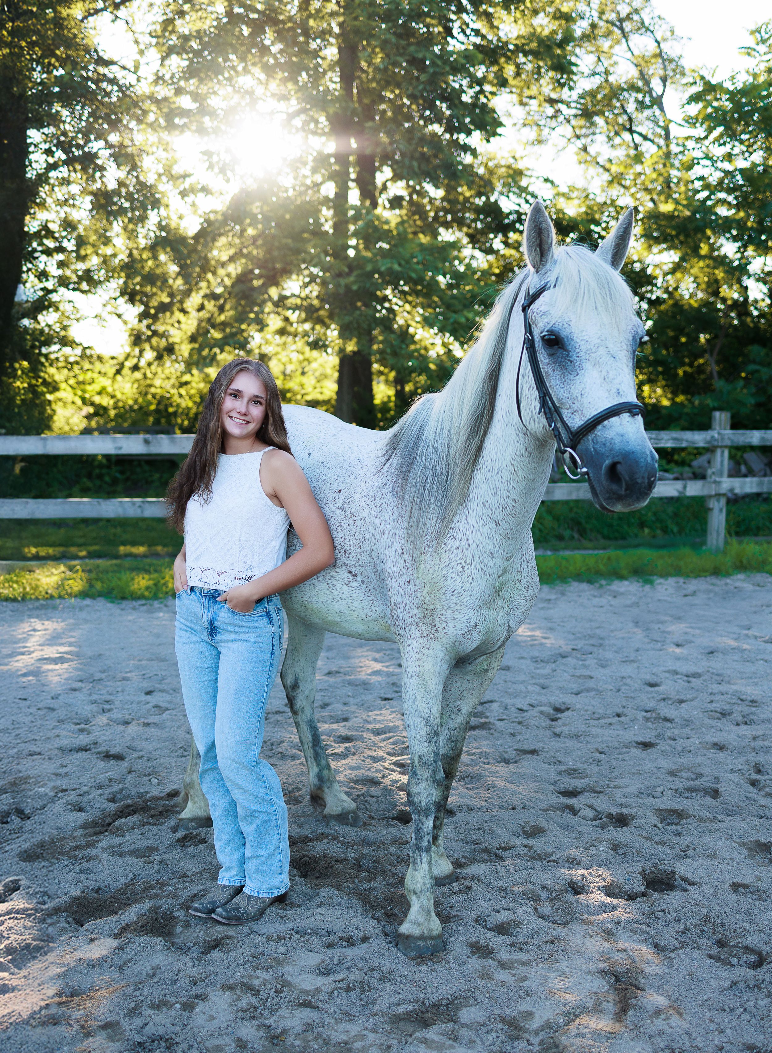 A dappled gray horse stands in a sandy arena at sunset while being photographed from different angles.