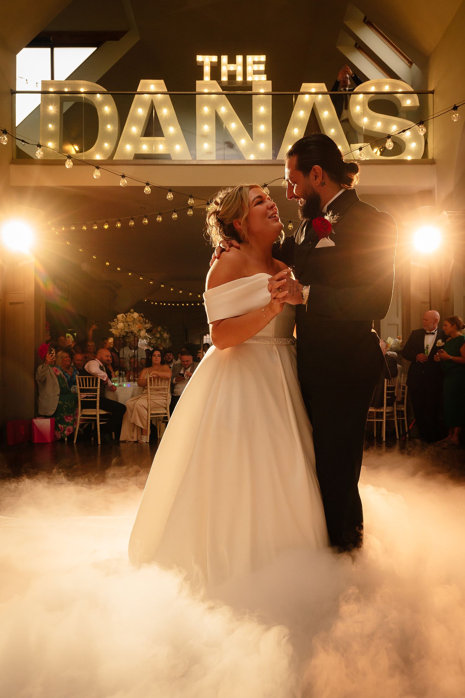 Newlyweds share their first dance under illuminated signage with fog effects on the dance floor.