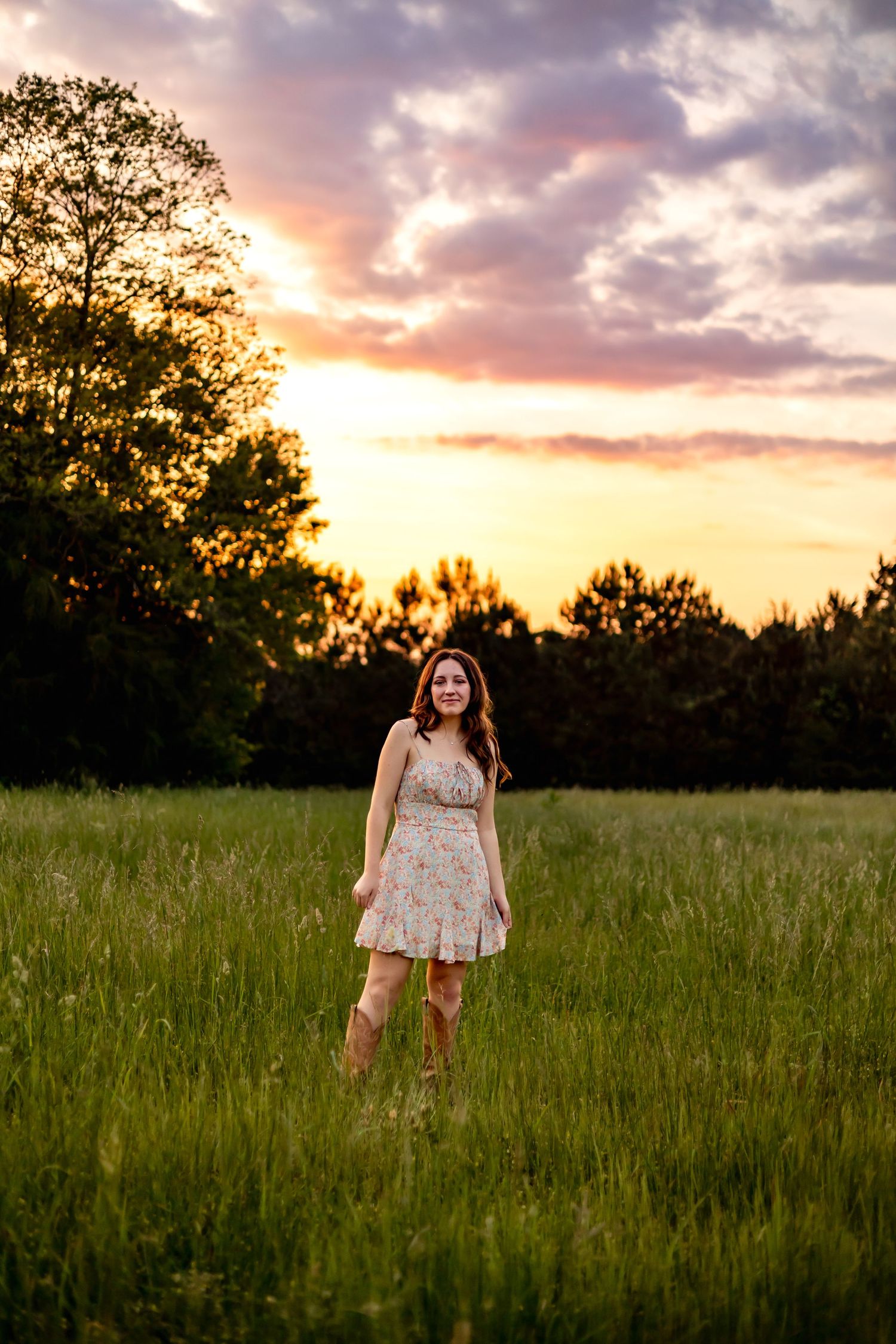 Person in floral dress standing in grass field during dramatic purple sunset.