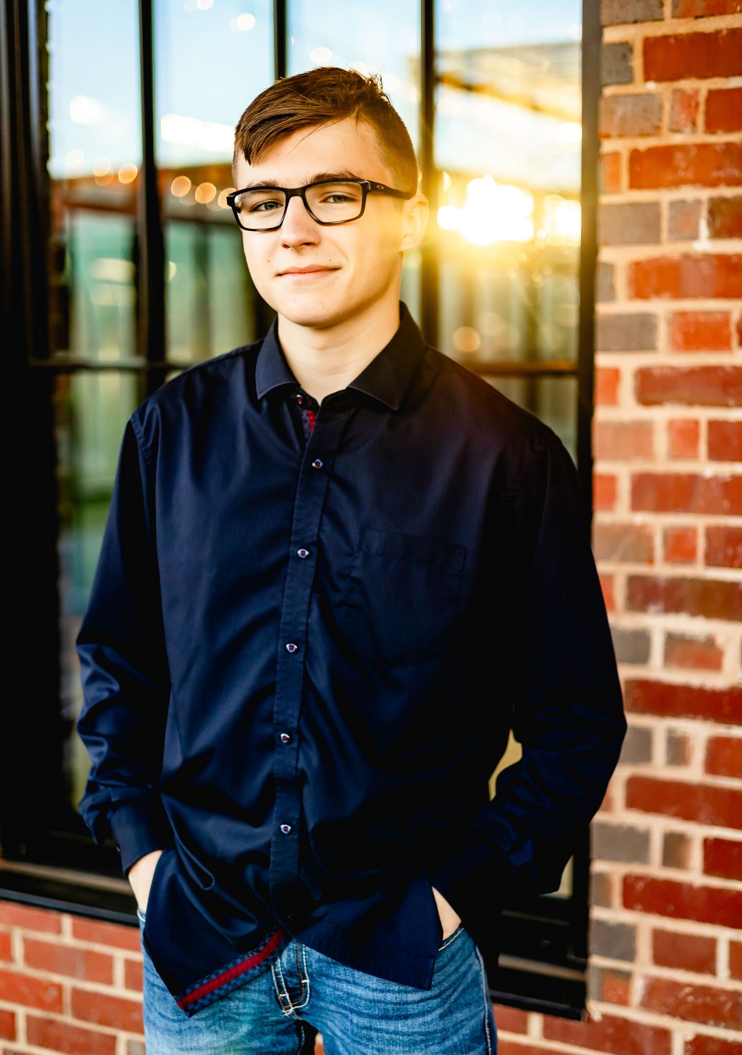 Person in navy button-down shirt standing against brick wall with sunset lighting.