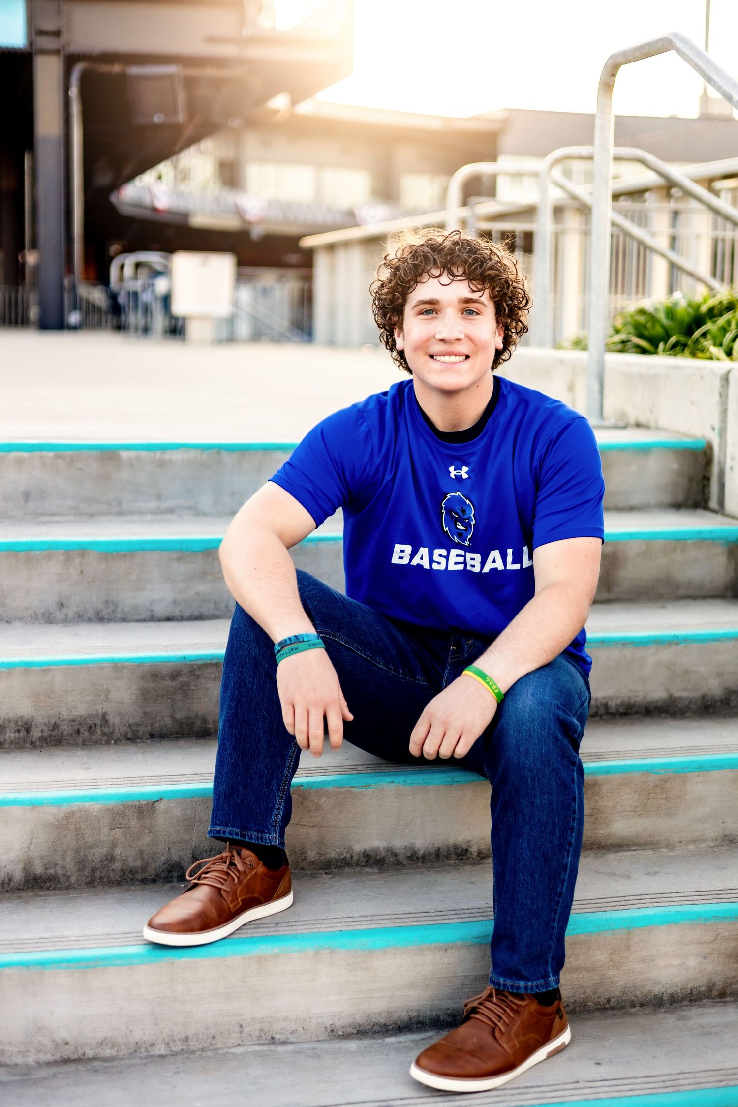 Person in blue baseball shirt sitting on concrete steps outdoors.