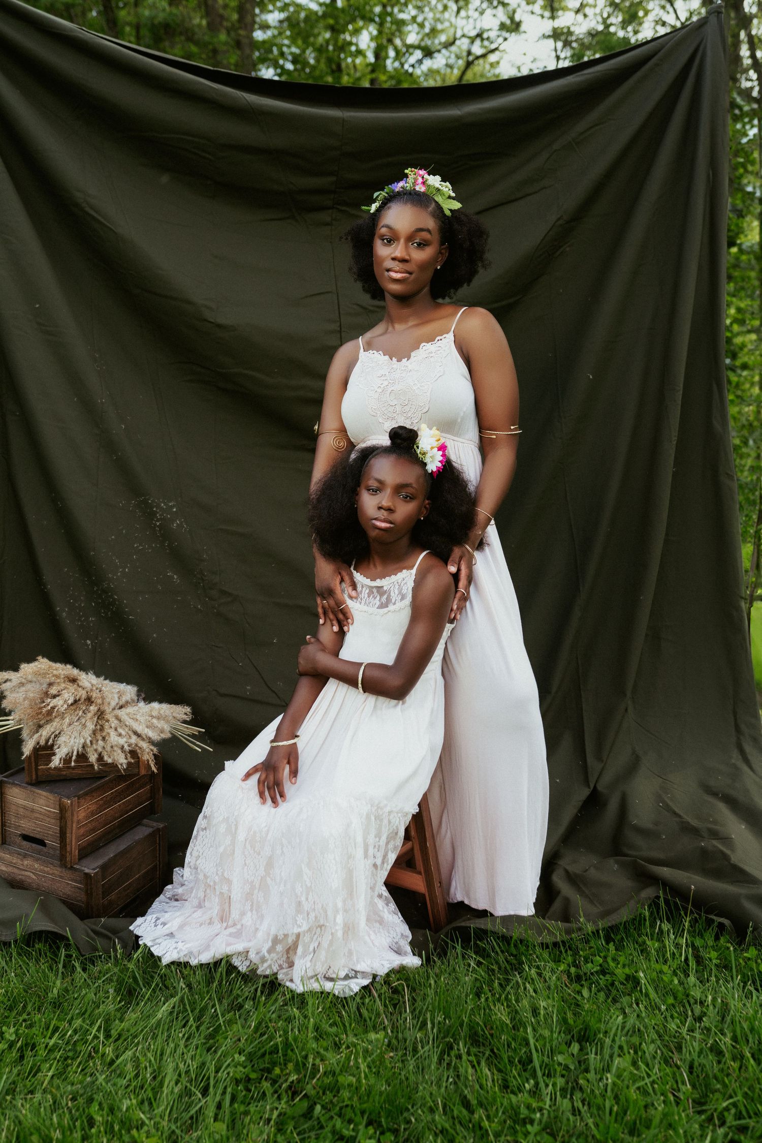Mother and daughter in matching white lace dresses posing before dark green backdrop outdoors.