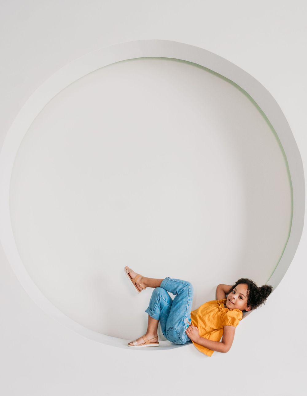 Person in yellow shirt and blue pants lies down on the edge of a circular white space creating a minimalist composition.
