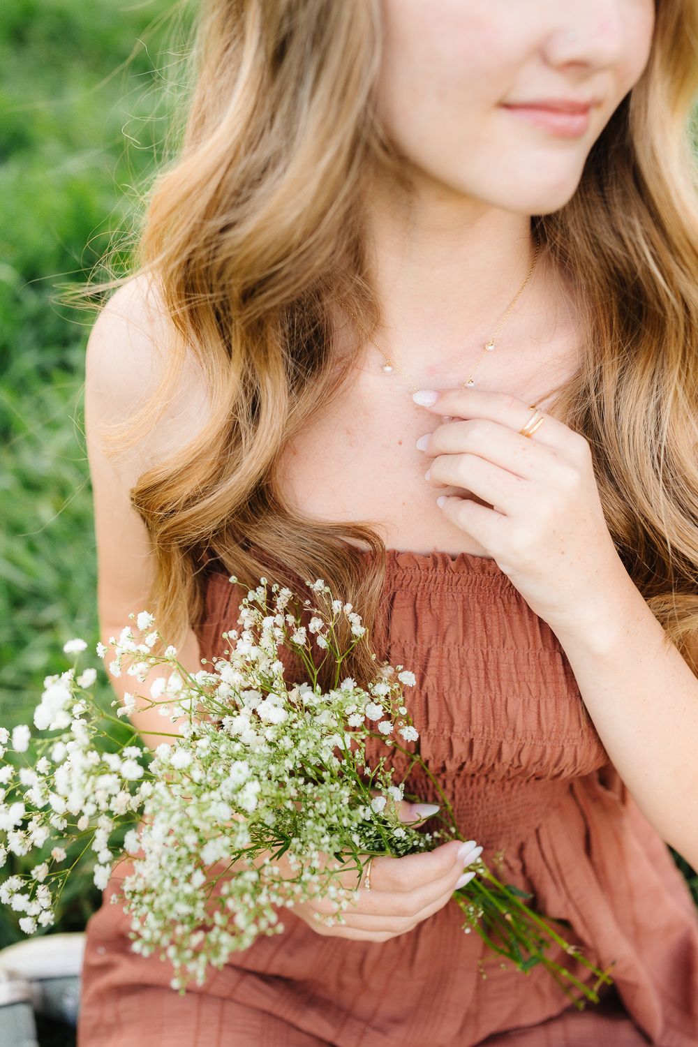 Dreamy outdoor portrait with baby's breath flowers and a brown ruched dress against green foliage.