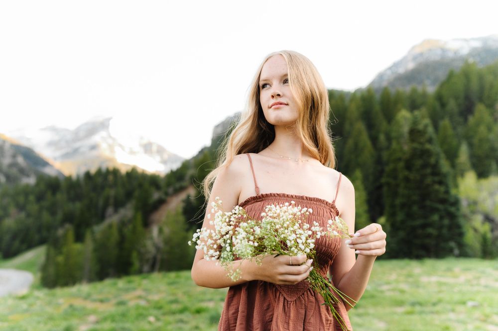 Portrait in mountain meadow wearing rustic dress and holding delicate wildflowers.