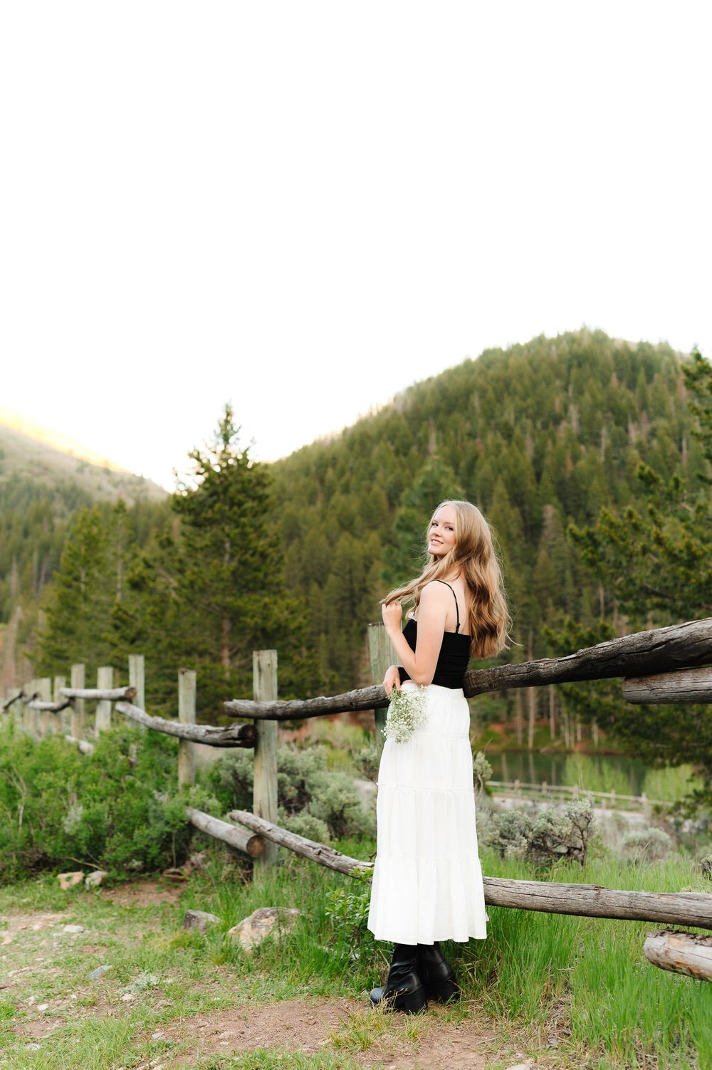 Scenic mountain photoshoot with rustic wooden fence and evergreen forest.