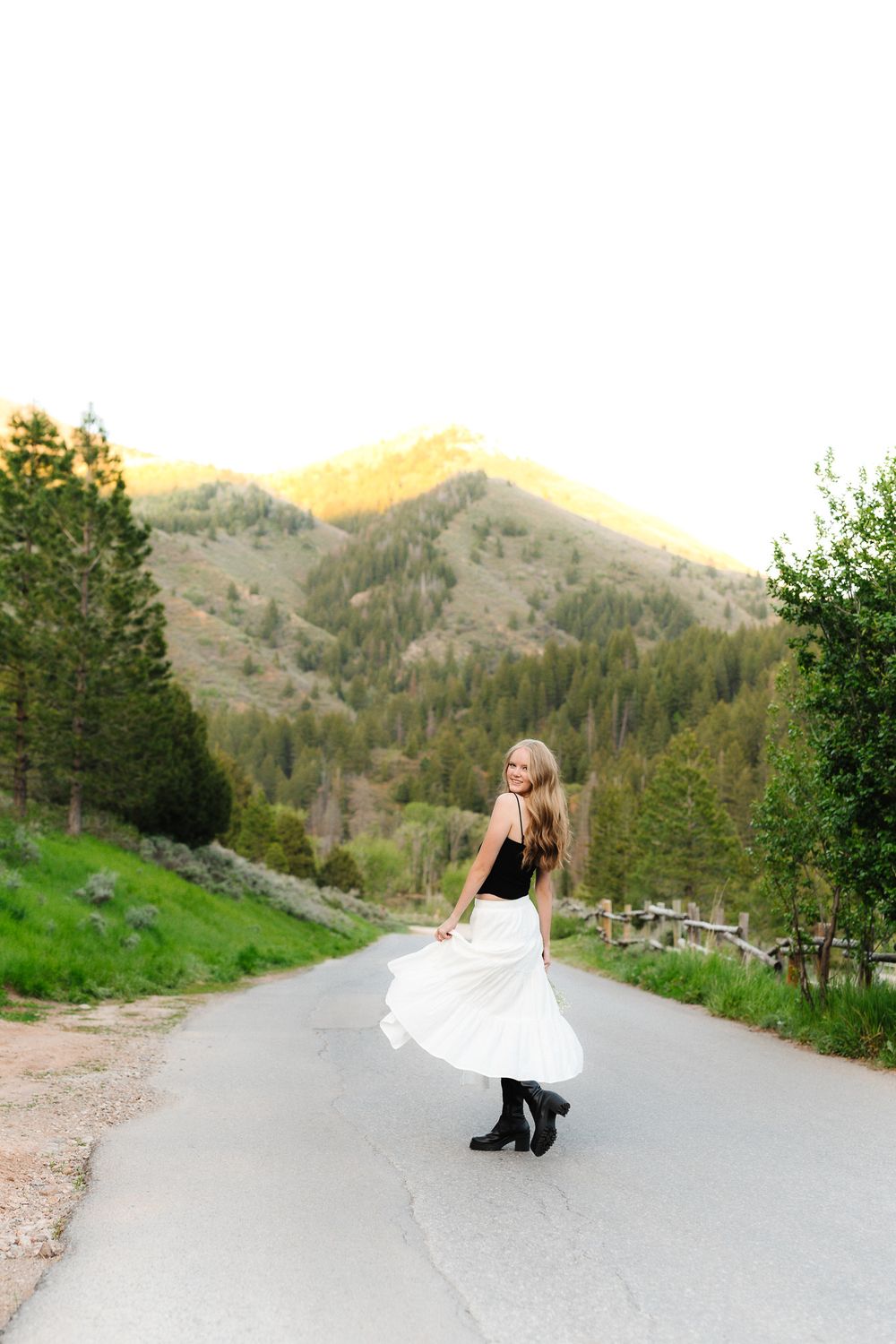 White dress twirling on mountain road with scenic mountain backdrop.
