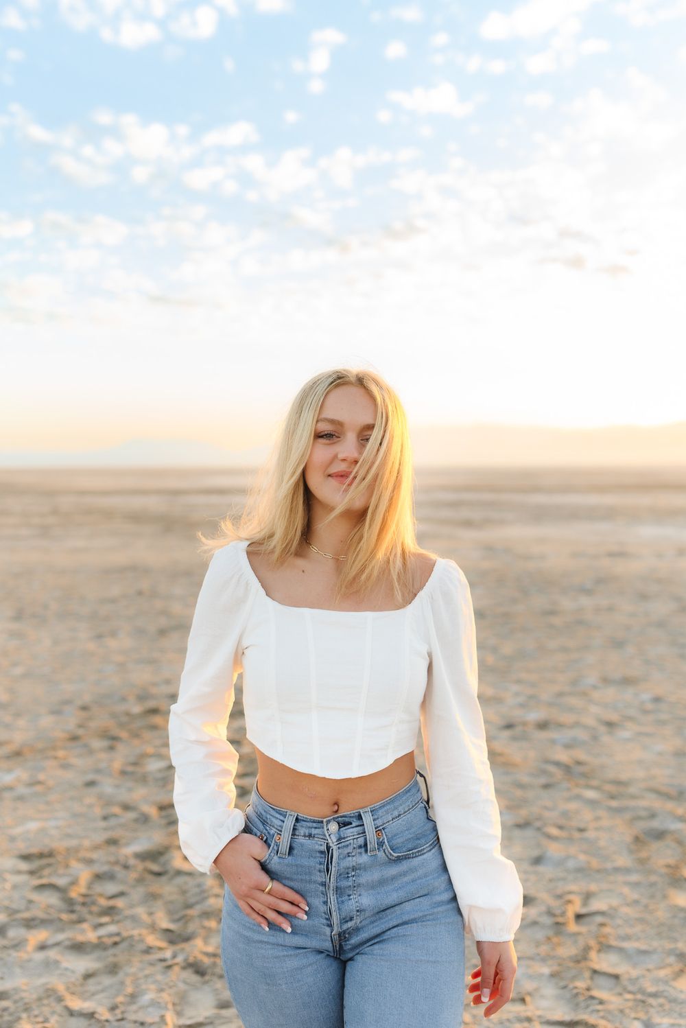 Person in white crop top and jeans poses in desert setting during golden hour.