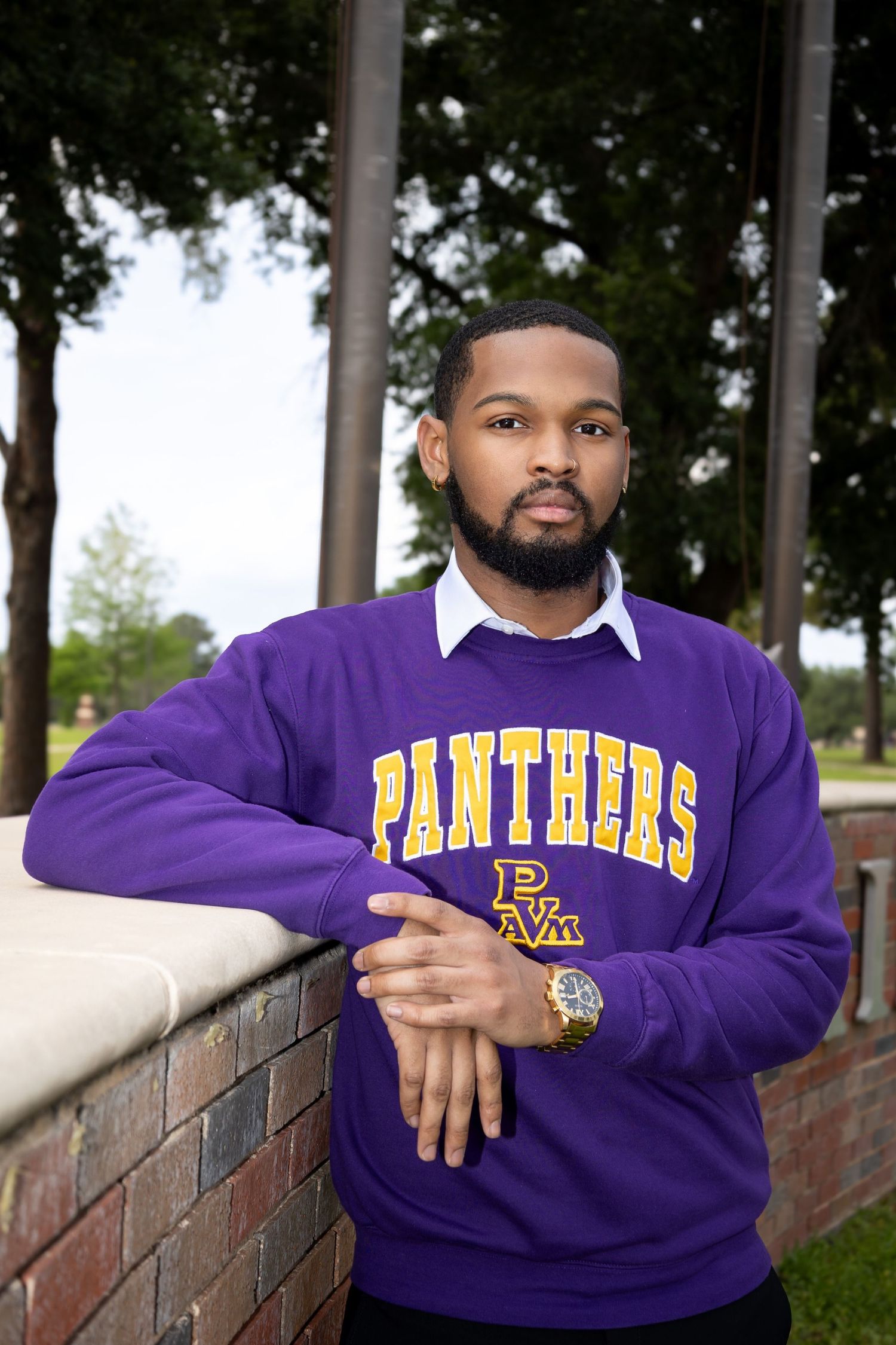 Person wearing purple Panthers university sweatshirt poses against brick wall outdoors.