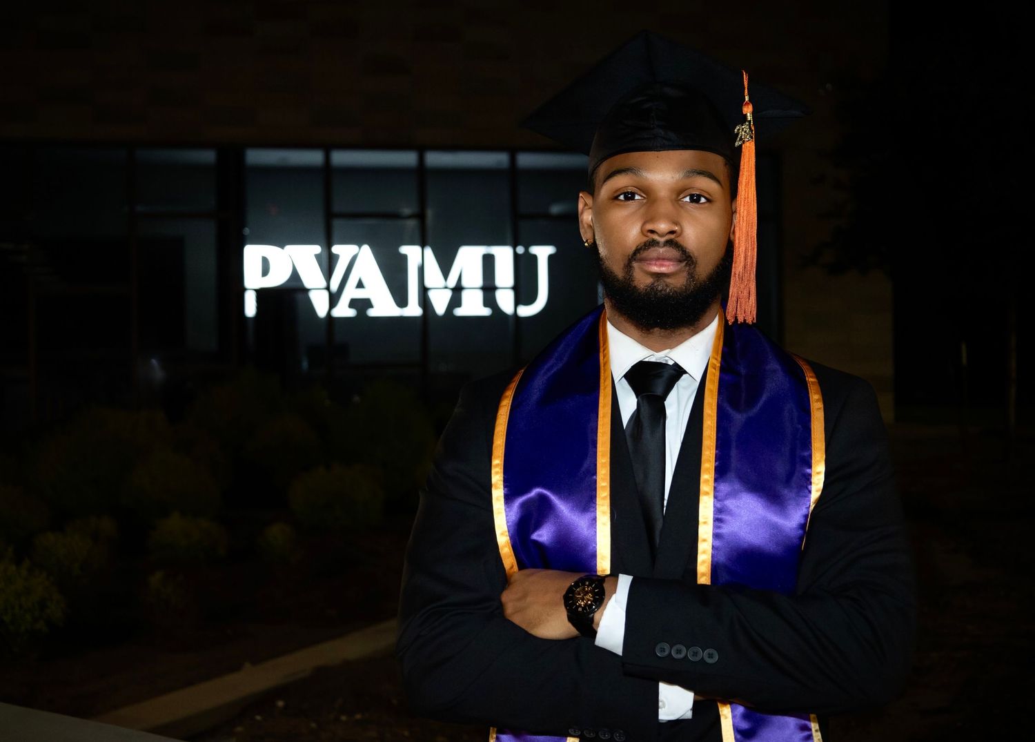 Graduate in academic regalia poses at night with FAMU sign illuminated in background.