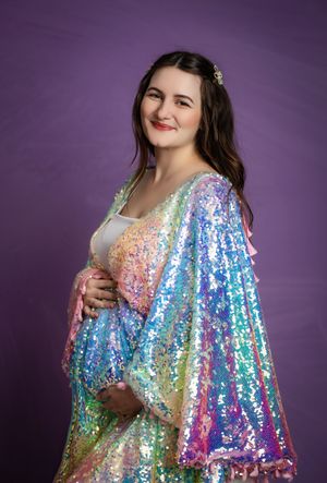 A woman in a shimmering rainbow sequin dress poses against a purple backdrop in a glamorous fashion photoshoot.