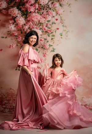 Elegant matching pink dresses with flowing ruffles against a romantic floral backdrop with pink roses and blossoms.