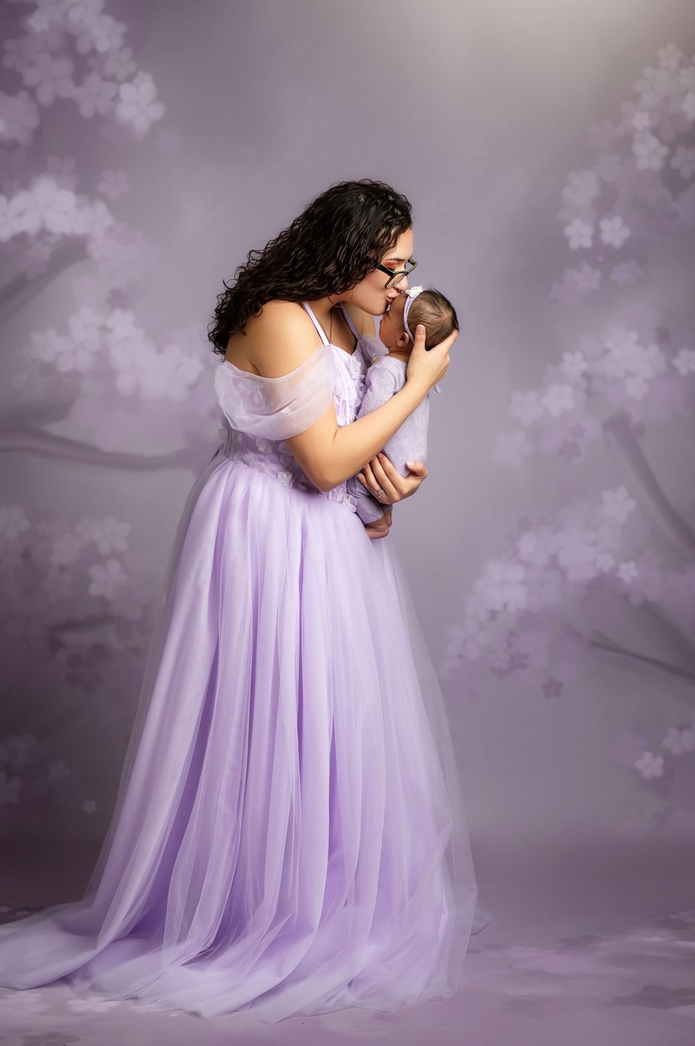 A flowing lavender tulle gown is photographed in a dreamy studio setting with soft lighting and floating floral elements.