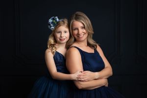 Portrait of a parent and child wearing matching navy blue formal dresses against a black background.