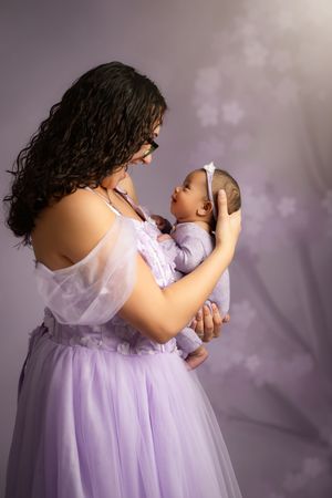 A series of photos showing a person in a flowing lavender dress holding and feeding a baby in a soft, dreamy setting.
