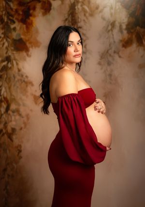 Artistic maternity photo featuring an off-shoulder deep red gown against a dreamy brown and cream backdrop.
