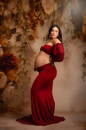 A maternity photo series showing a person in a burgundy dress against a floral backdrop in dreamy studio lighting.
