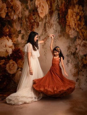 Two figures in flowing dresses, one white and one rust-colored, dance together against a romantic floral backdrop.