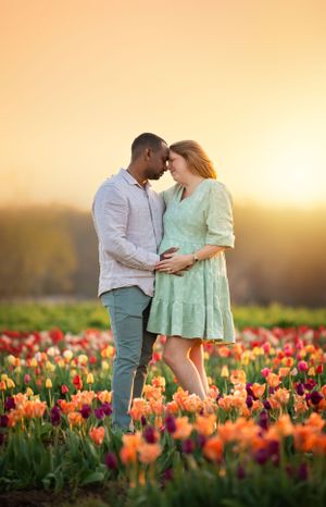 A couple shares an intimate moment in a field of orange and red tulips at sunset, with the woman wearing a mint green dress.