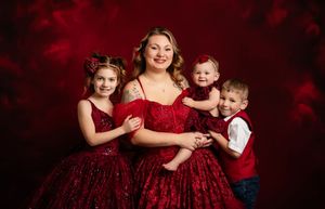 A family in coordinating deep red velvet holiday dresses and outfits poses together for festive portraits.