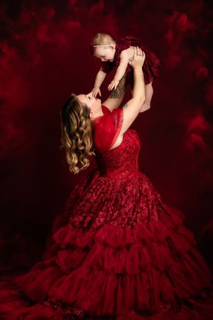 A figure in a luxurious deep red ruffled ball gown poses against a dark dramatic background.