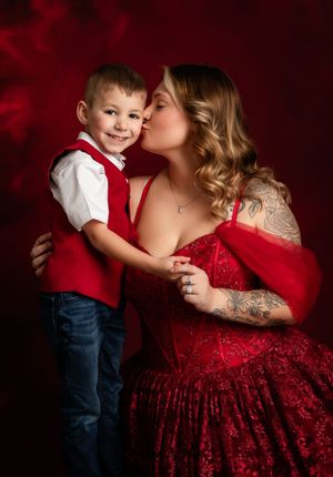 A tender moment captured in a red-themed portrait session with matching red dress and vest against a dark background.