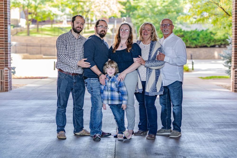 Multi-generational family of six smiling together outdoors on a brick walkway.