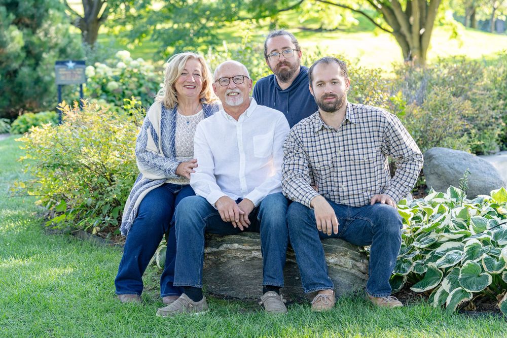 Family of four poses on stone bench in lush garden setting for outdoor portrait photography.