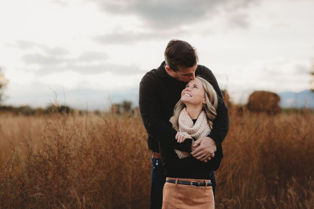 A couple shares an intimate embrace in a golden field during sunset with moody autumn skies overhead.
