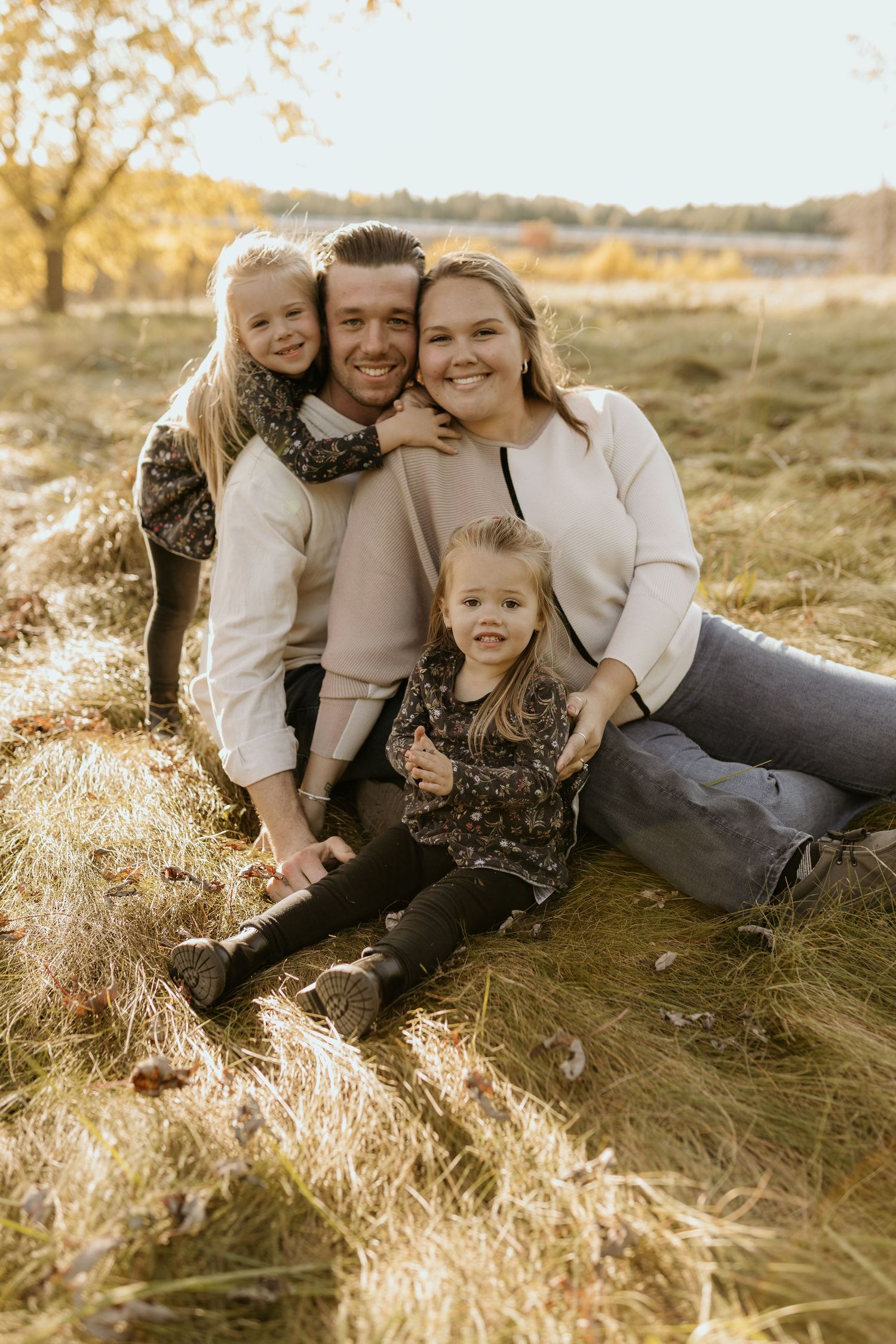 Joyful family portrait with parents and children sitting in golden autumn field at sunset.