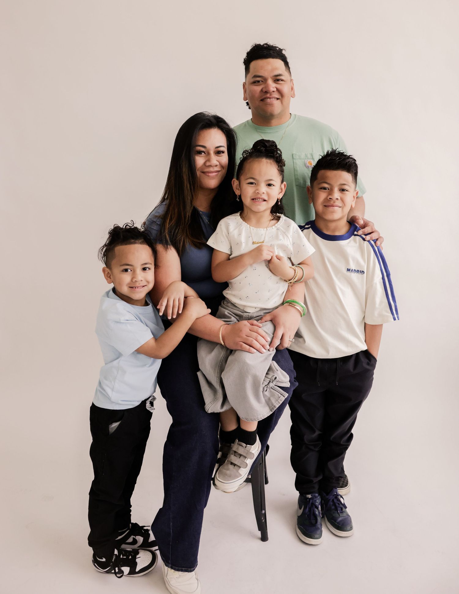 A happy family of five posing together in a studio, with parents and three young children smiling warmly.