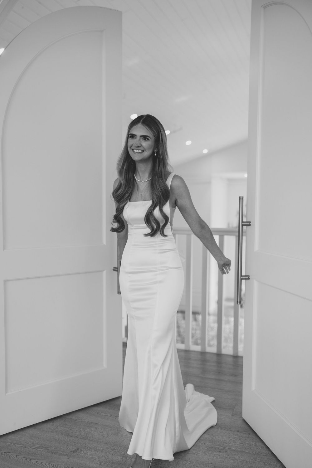 Black and white portrait of bride in fitted wedding dress standing in modern doorway.