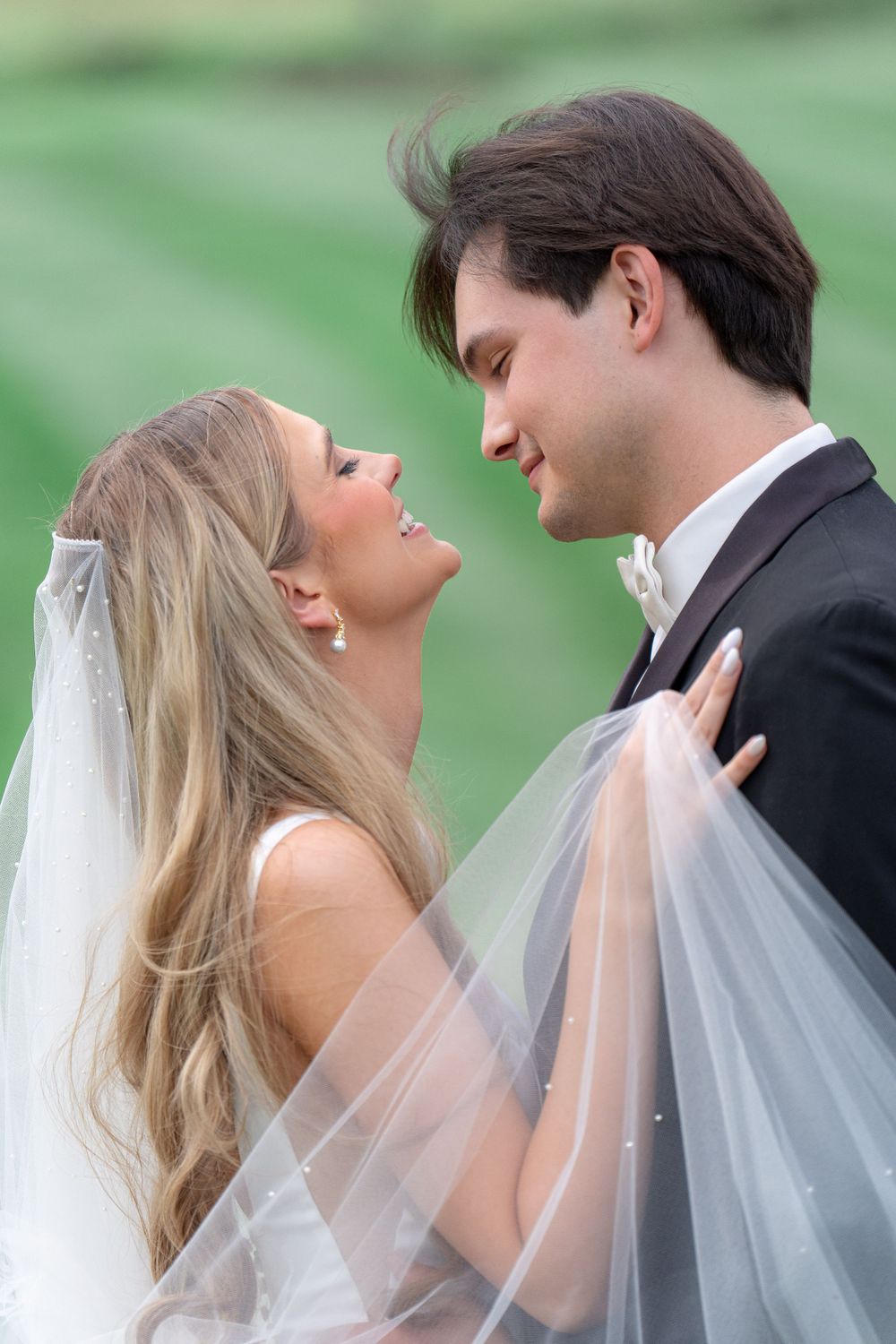 Romantic moment between newlyweds with bride's veil flowing in outdoor setting.
