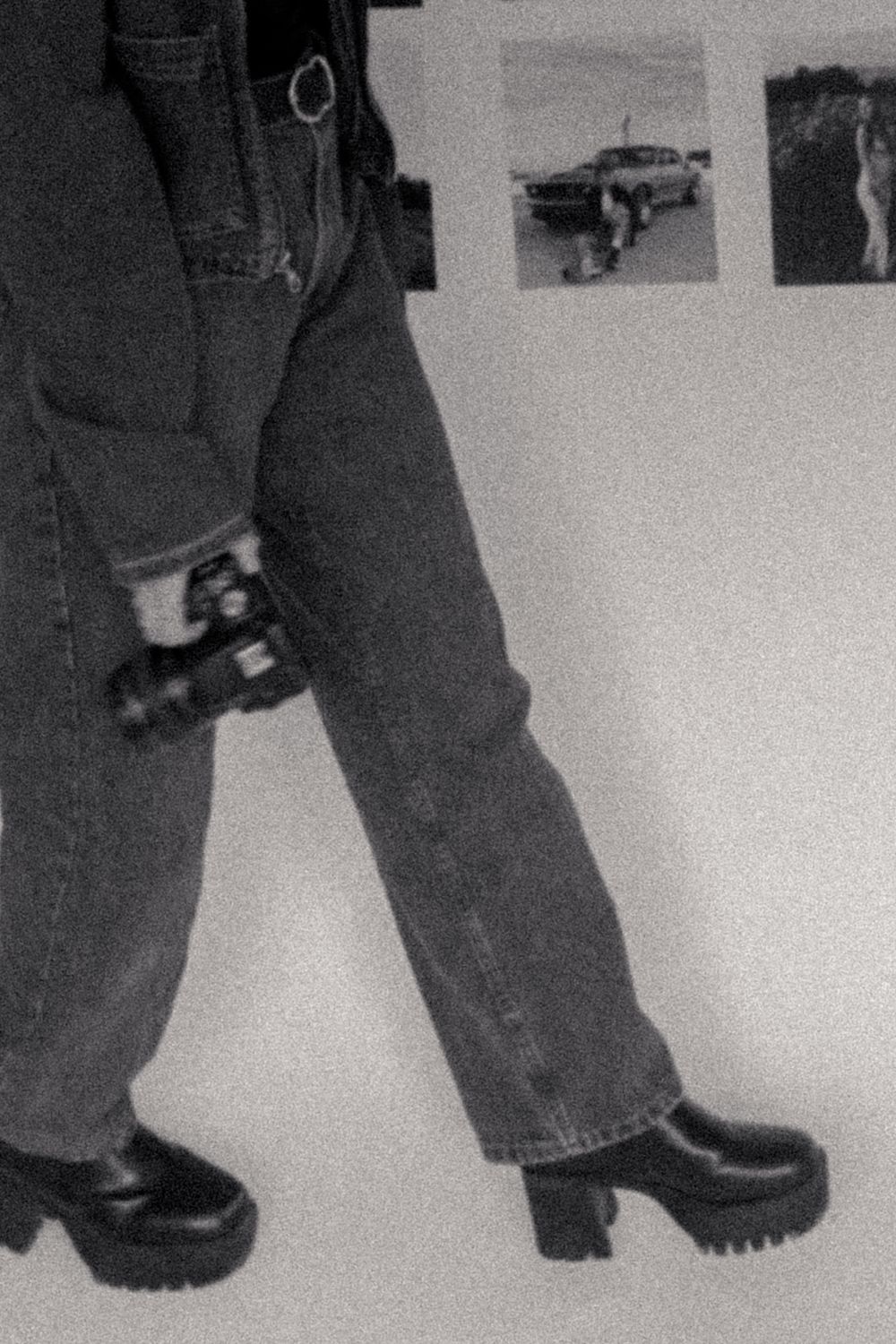Close-up black and white photo of legs wearing baggy jeans and black shoes walking in sequence across a white surface.