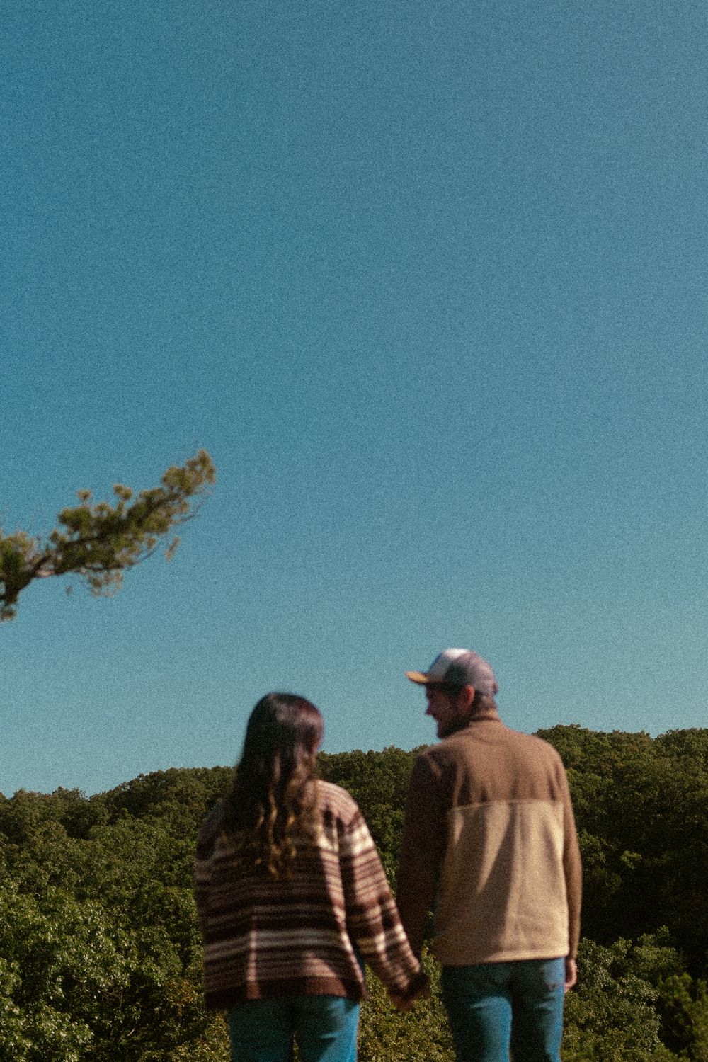 A couple enjoys a peaceful moment overlooking a lush green forest beneath a bright blue summer sky.