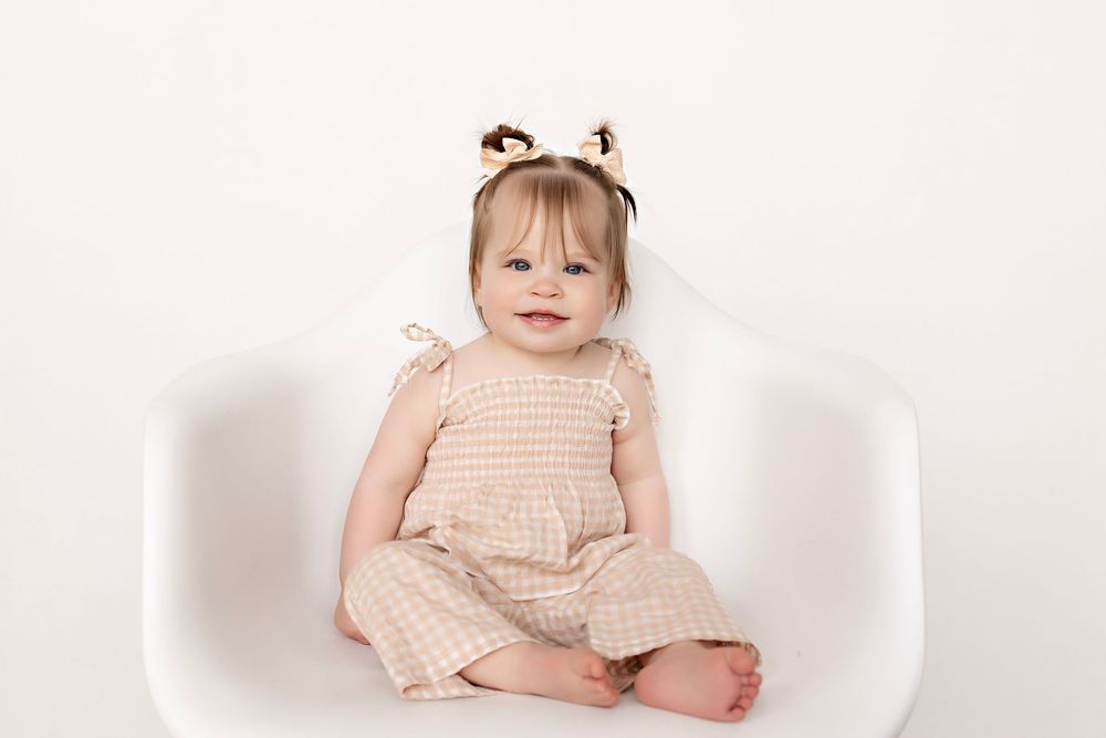 Baby in peach colored dress sits and smiles against white background in studio photography.  Kendall Kuss Photography Watertown WI