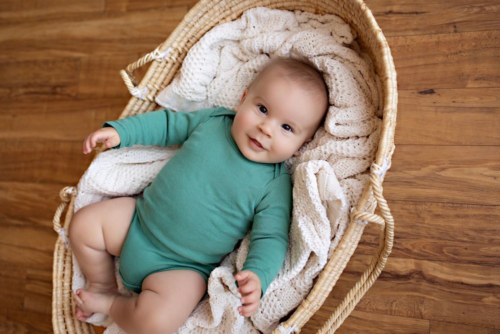 Baby in teal onesie lying in woven basket with cream blanket on wooden floor. Kendall Kuss Photography baby photos at studio in SE Wisconsin