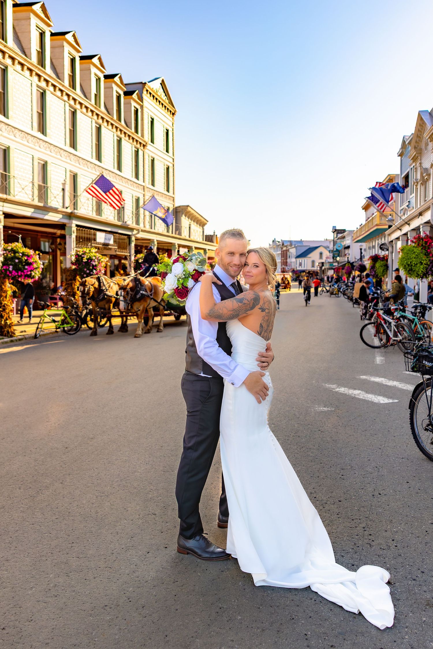 A couple in wedding attire embraces on Mackinac Island's Main Street with historic buildings and bicycles in the background.