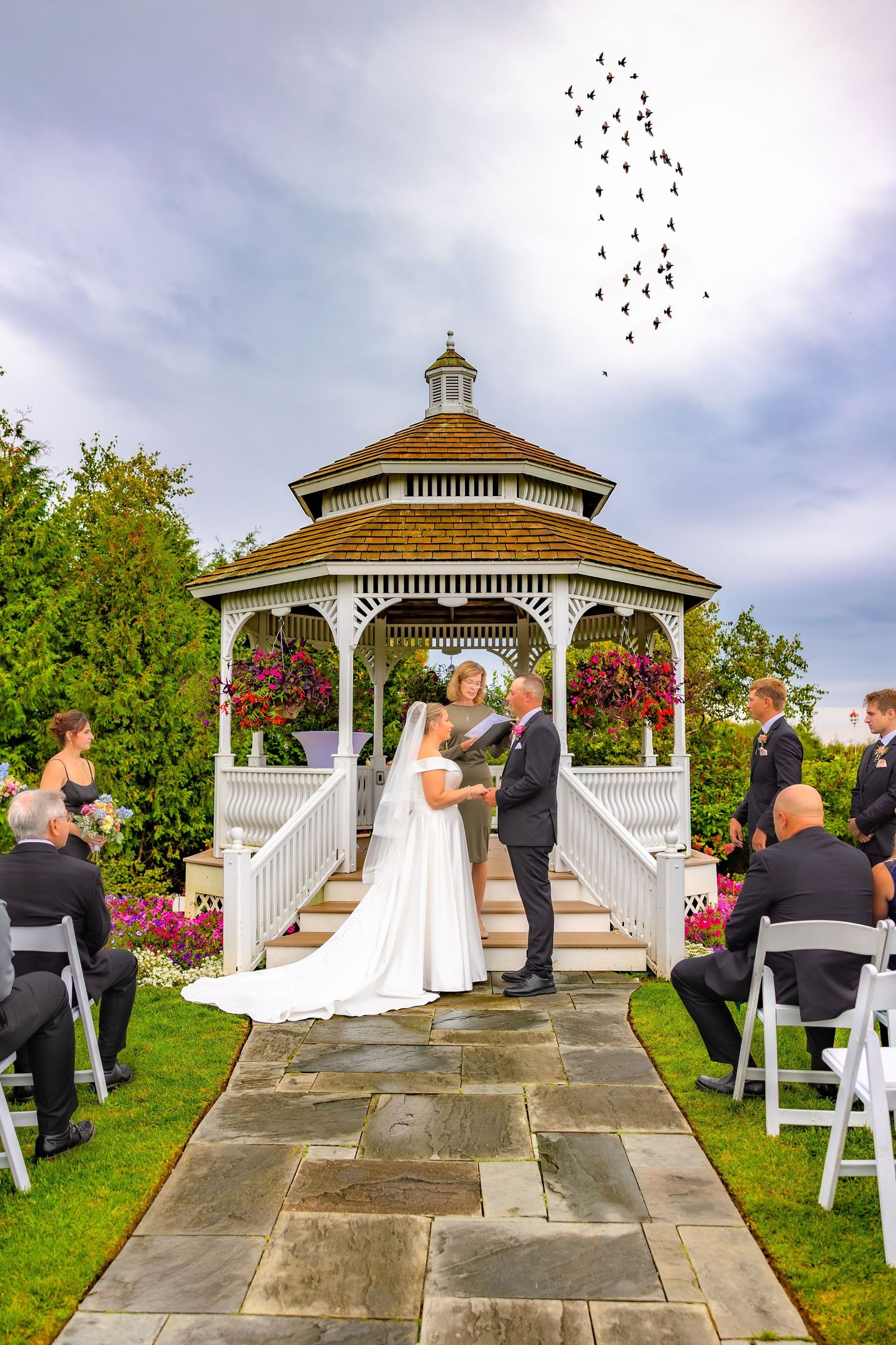 Outdoor wedding ceremony sequence at white gazebo with floral decorations and seated guests under cloudy sky.