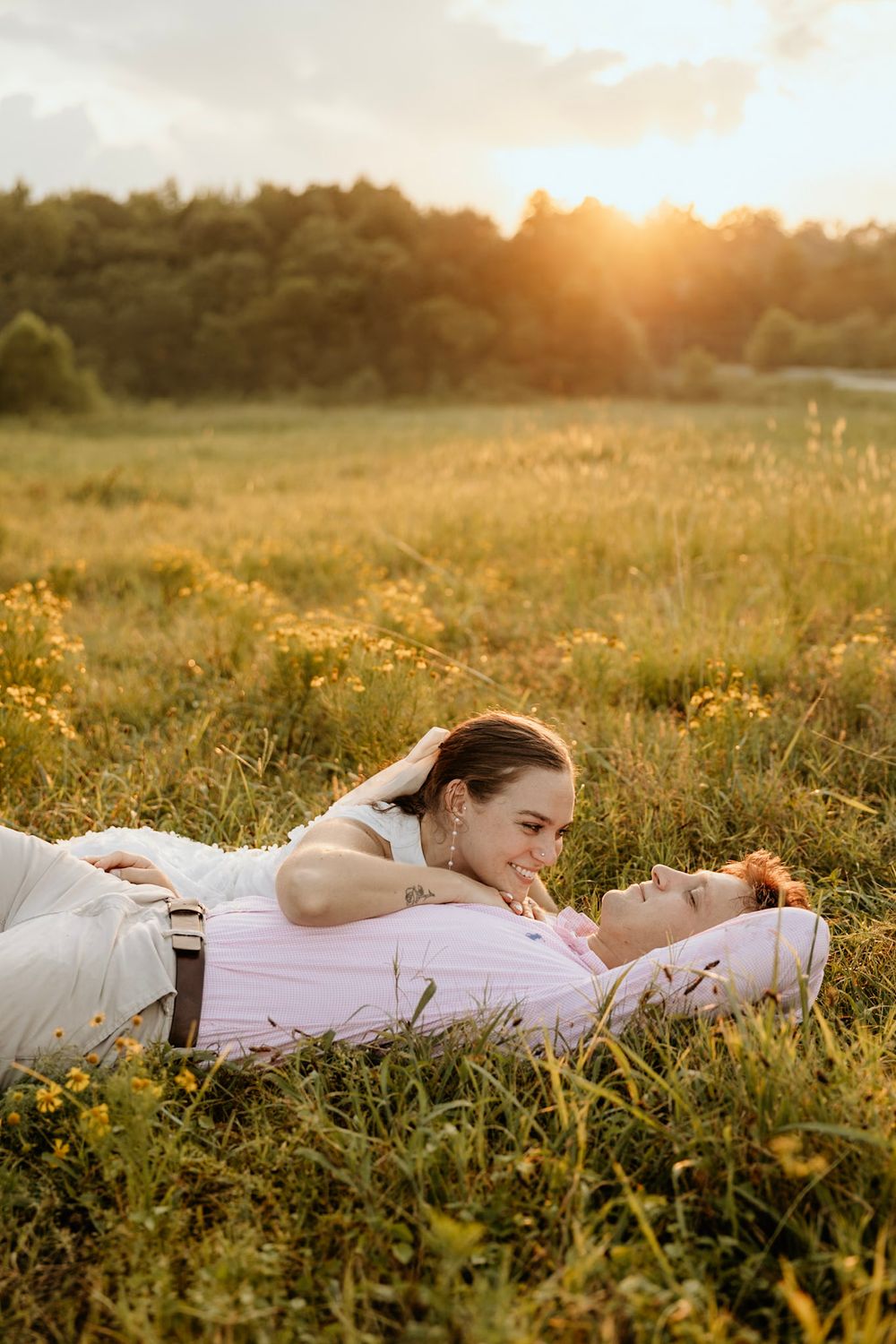 A couple relaxes in a golden wildflower field at sunset with soft lighting creating a romantic atmosphere.