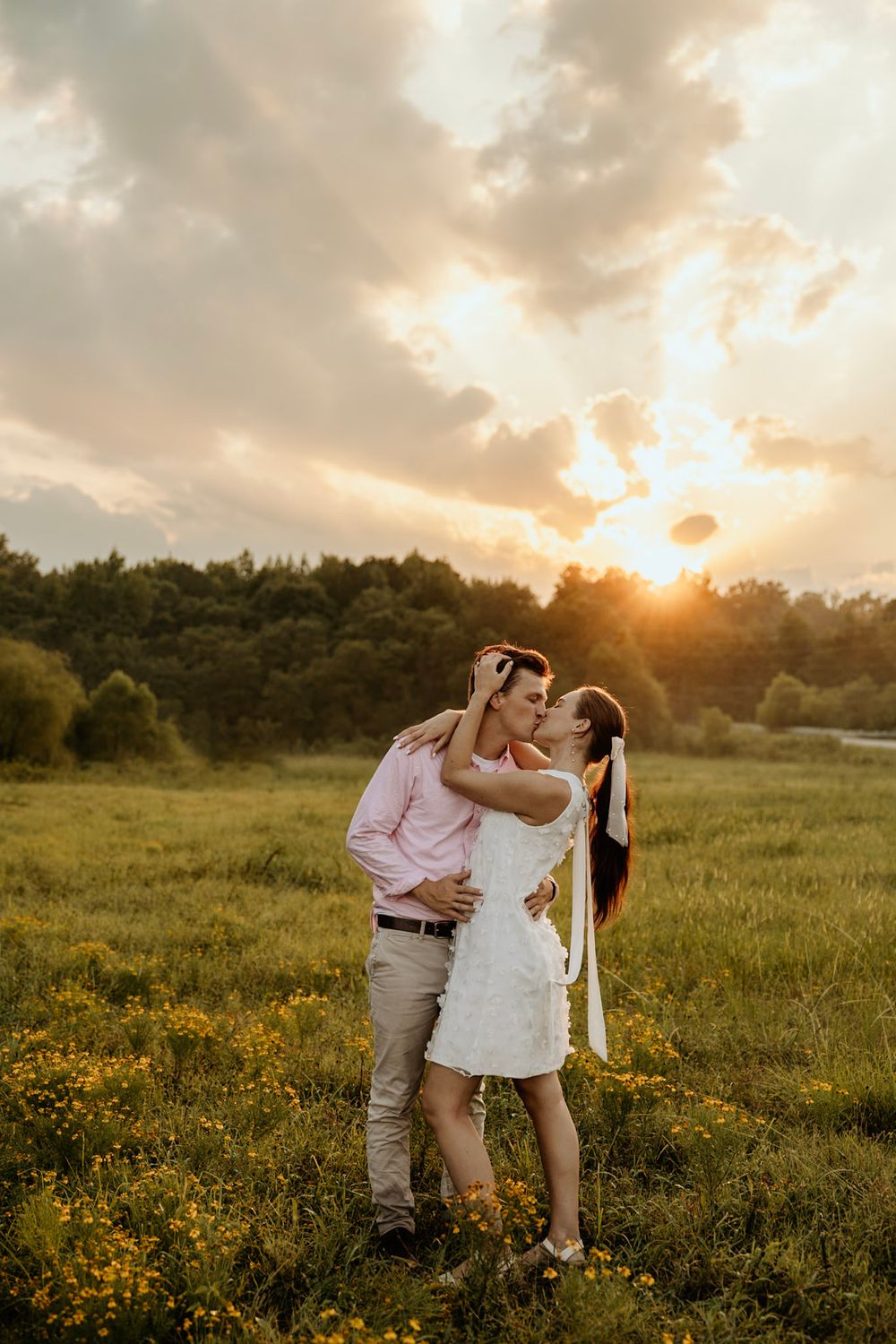 A romantic moment between two people standing in a field of yellow wildflowers during a glowing sunset.