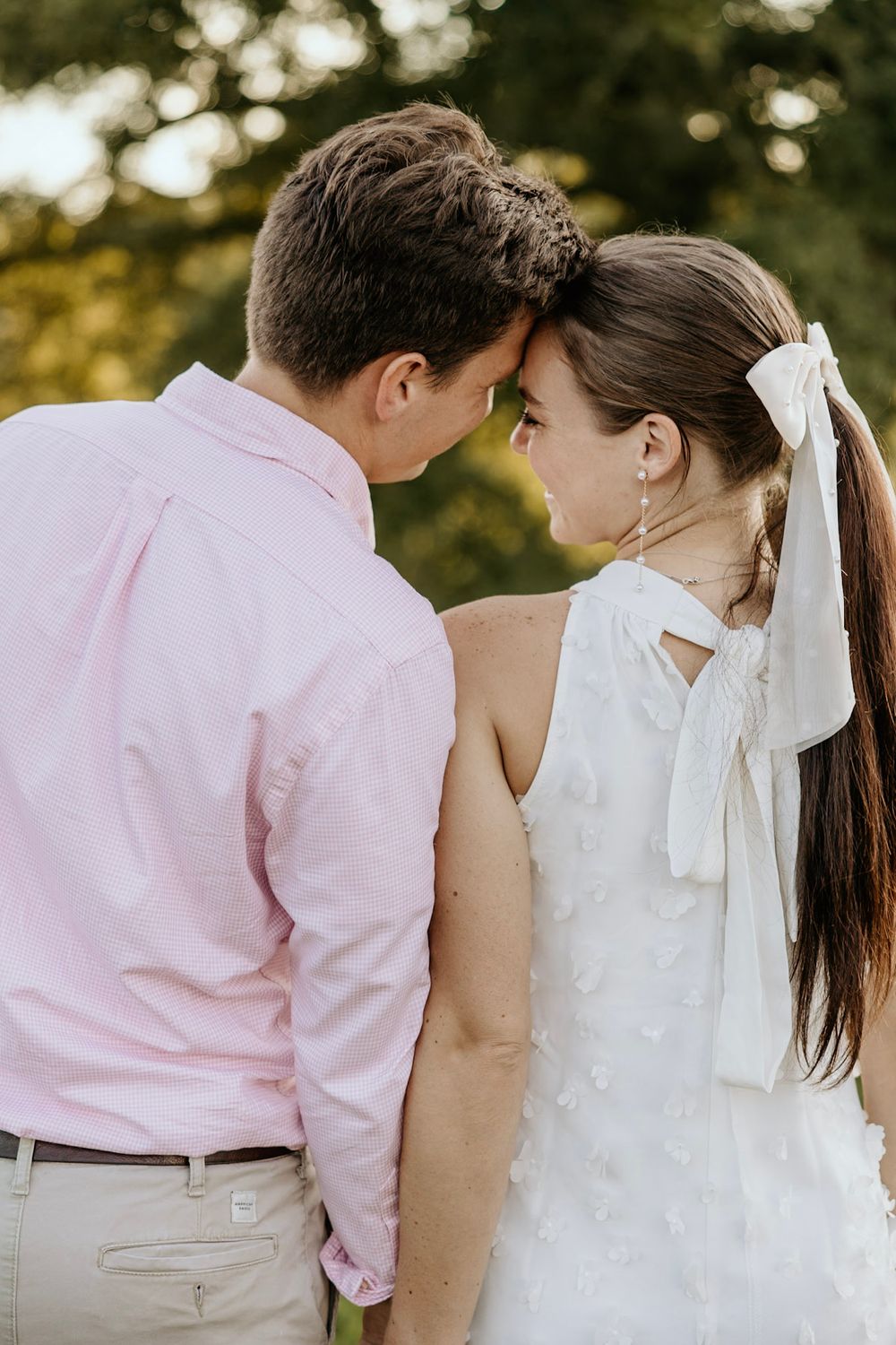 A tender wedding moment between a couple sharing an intimate pose outdoors with soft bokeh lighting in the background.