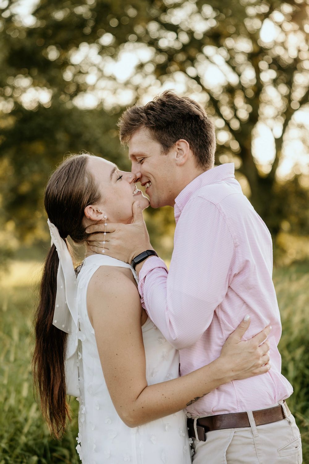 A romantic outdoor wedding portrait shows a couple embracing in a sunlit field during golden hour.